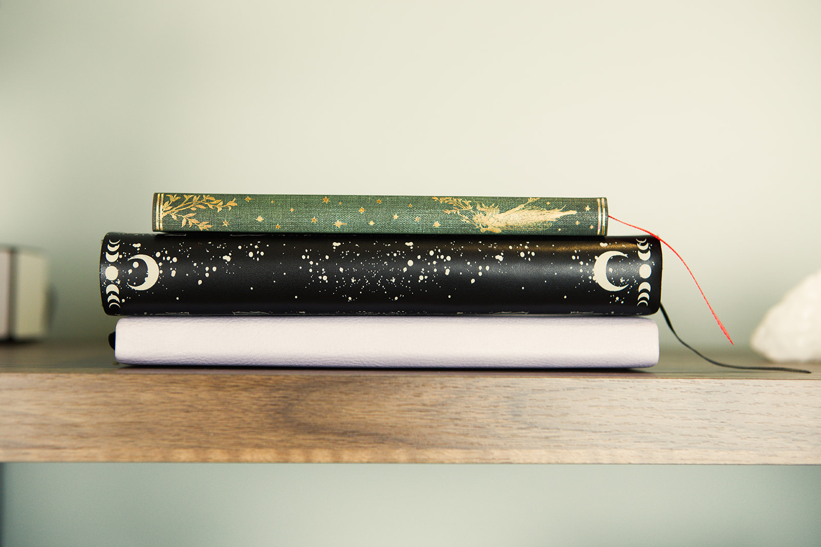 Three journals stacked on a wooden shelf, one with a red ribbon marker