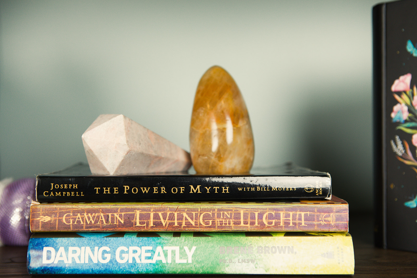 A stack of books beside warm colored crystals on a wooden shelf