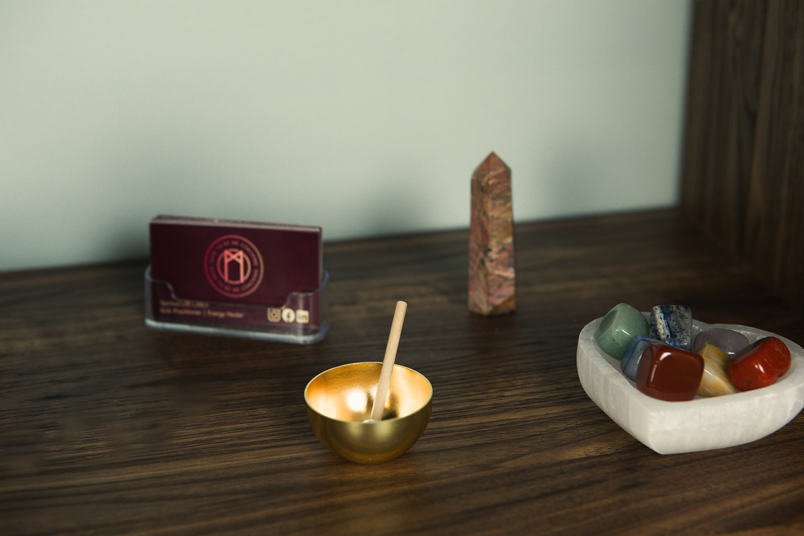 A small brass singing bowl, a crystal point and a dish of tumbled stones on the wooden shelf in Nina's space