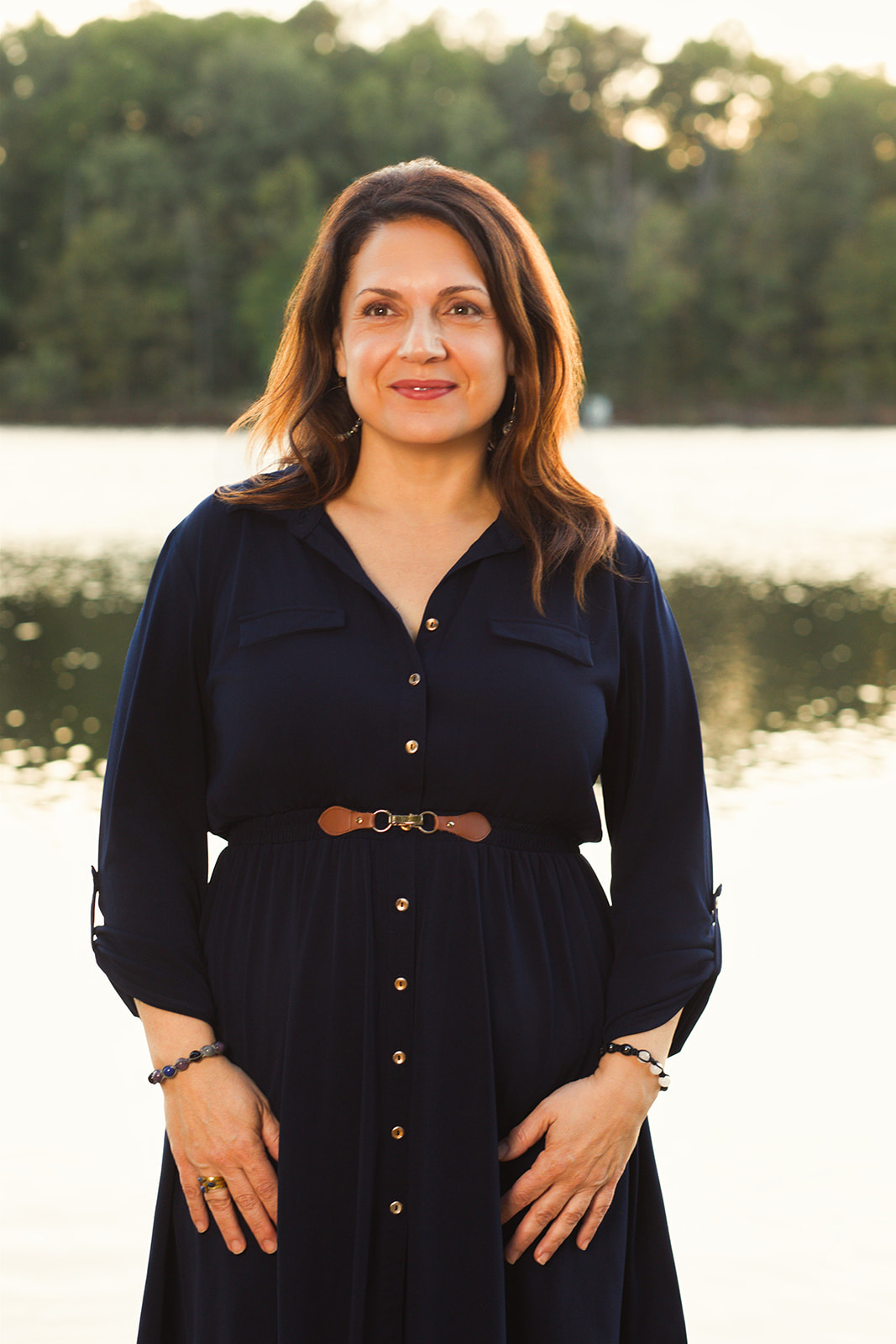 Nina standing peacefully beside a lake in a navy dress