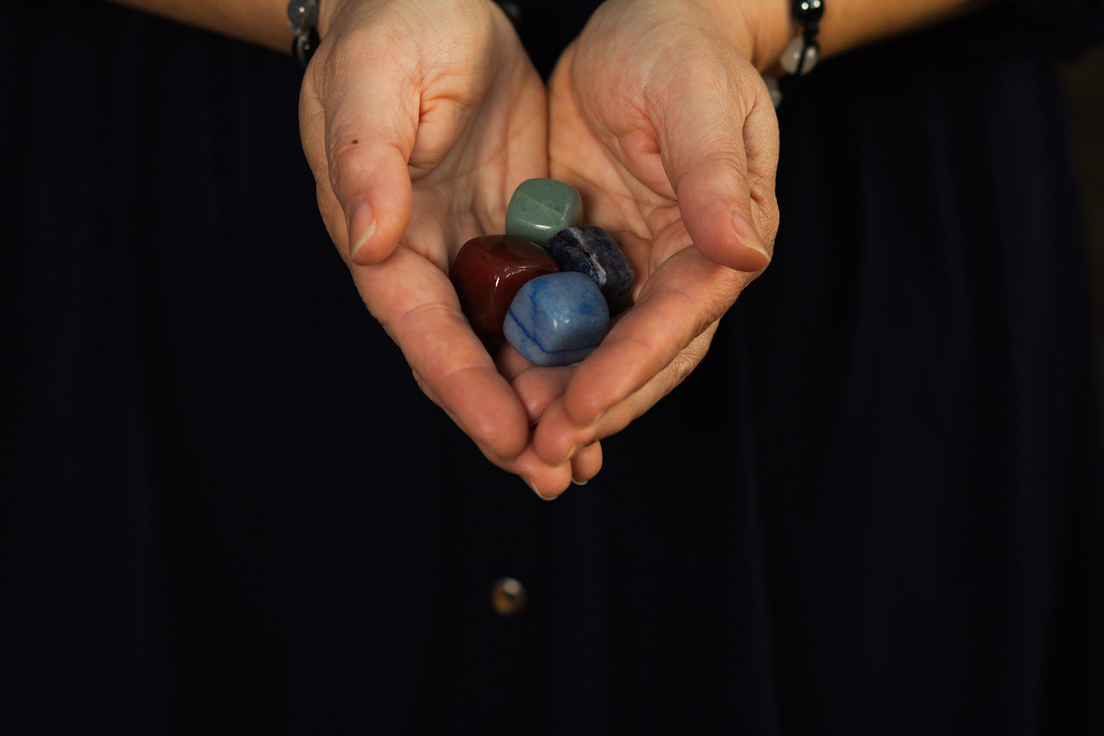 Two open hands gently holding small colored crystals