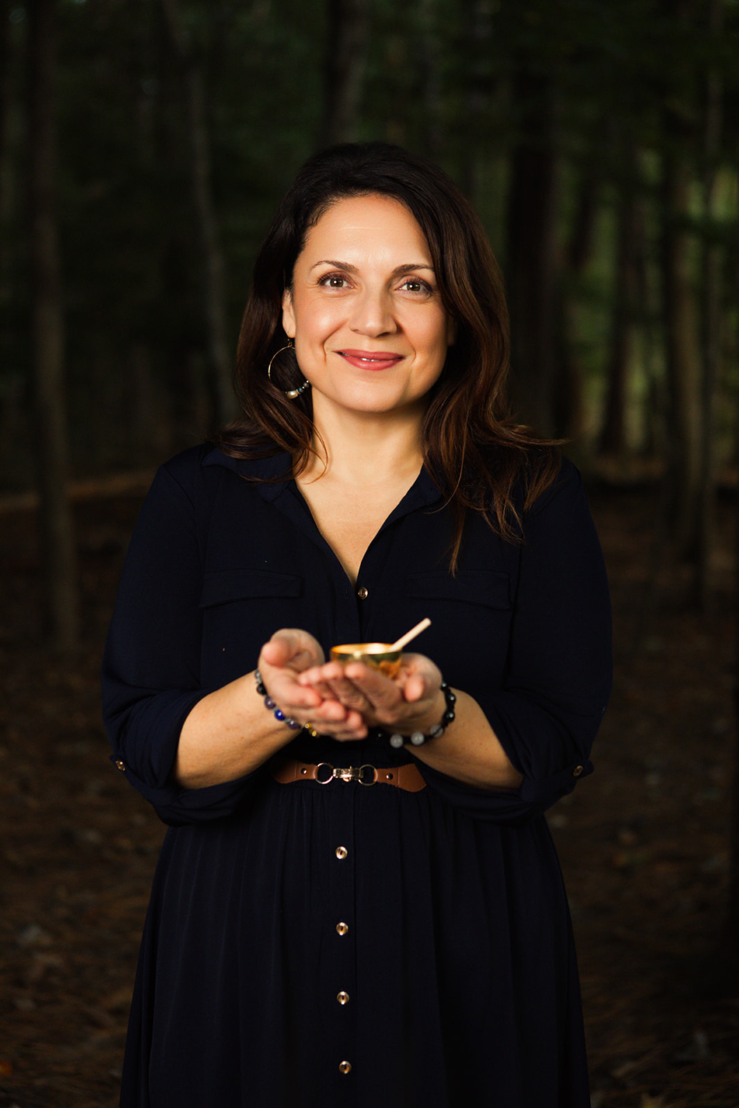 Nina Della Vecchia smiling softly in a dark forest, holding a small light in her hands