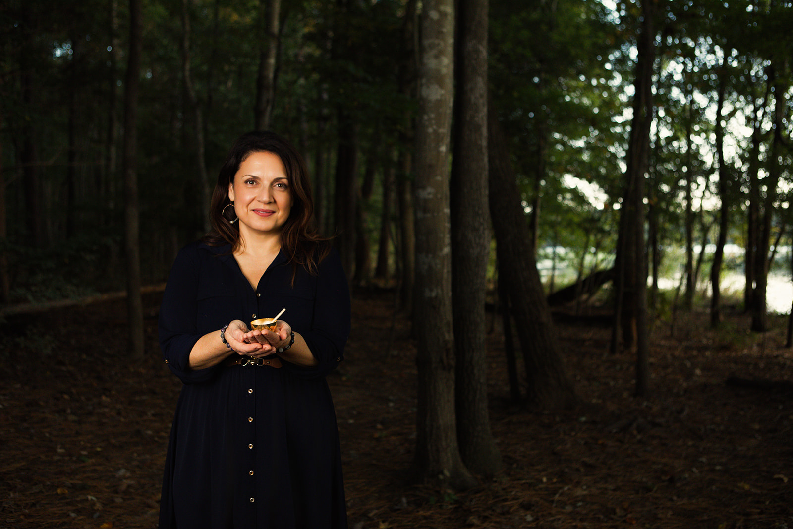 Nina standing in the woods at dusk, holding a small bowl in both hands