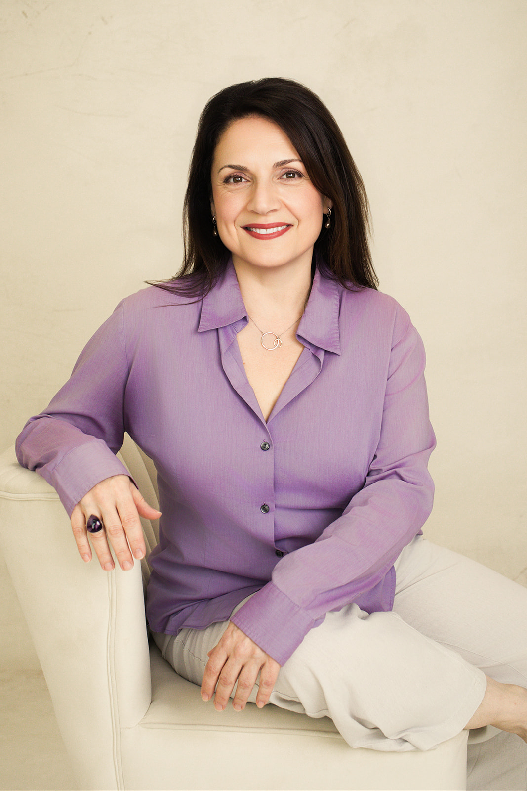 Nina Della Vecchia seated in a cream chair, smiling warmly