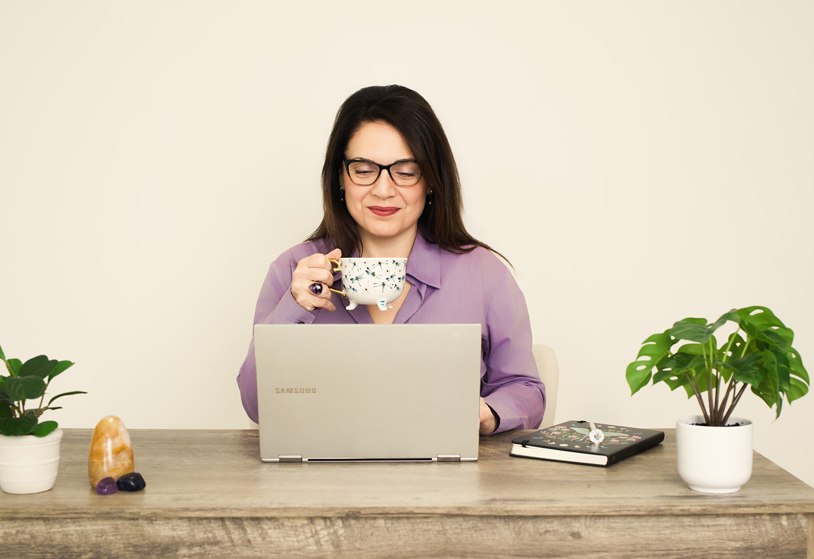 Nina pausing with a warm cup at her desk, laptop open beside her