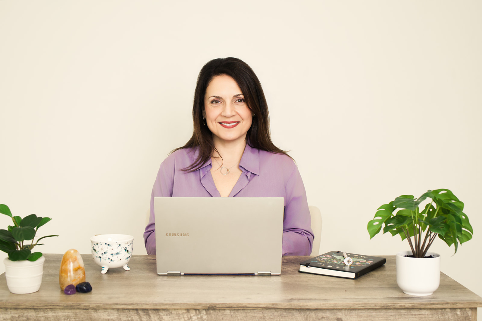 Nina smiling at her laptop during a virtual session, plants and warm light around her desk