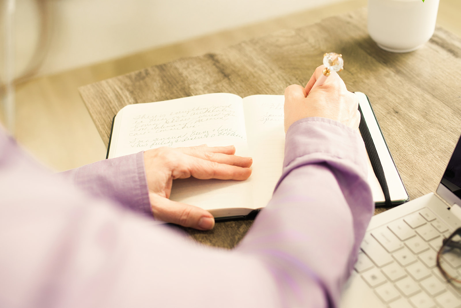 A hand resting on an open journal beside a cup of tea