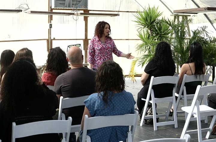 Nina speaking to a seated group at a workshop held in a bright greenhouse